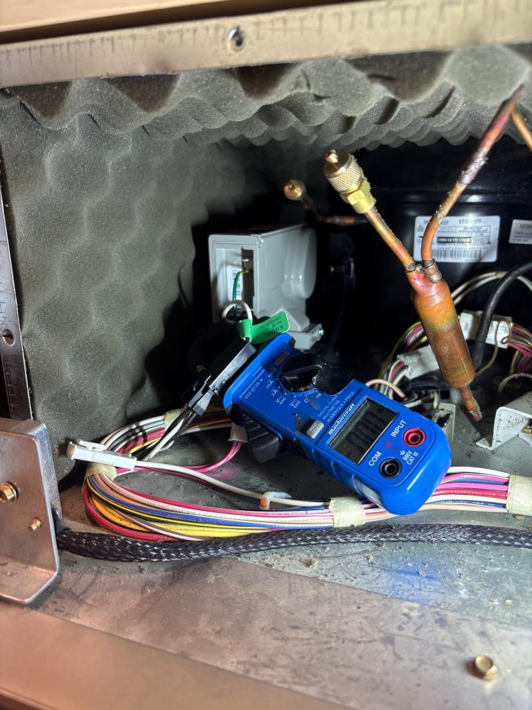 TechVill technician using a clamp meter to measure KitchenAid refrigerator compressor current after inverter box replacement in Bearspaw, Calgary
