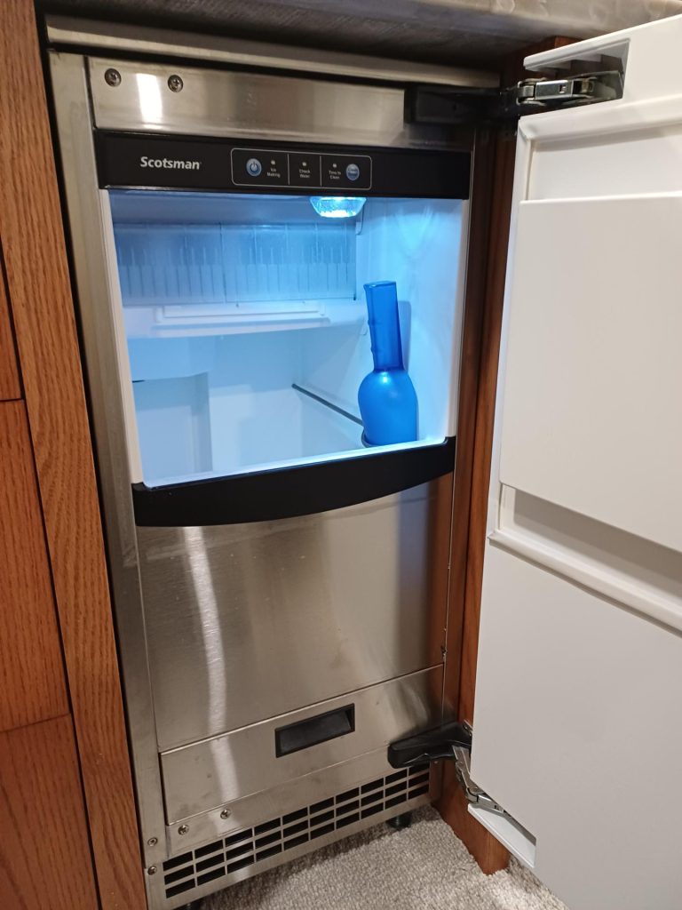 Stainless steel Scotsman SCCP50MB-1SS under-counter ice maker built into wood cabinetry in an Inglewood, Calgary kitchen, door open with the empty ice bin lit blue