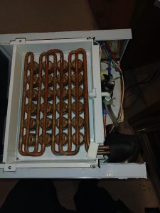 Top-down view inside the Scotsman under-counter ice maker showing the copper evaporator grid that freezes the ice, alongside the component bay and wiring during diagnosis in Calgary