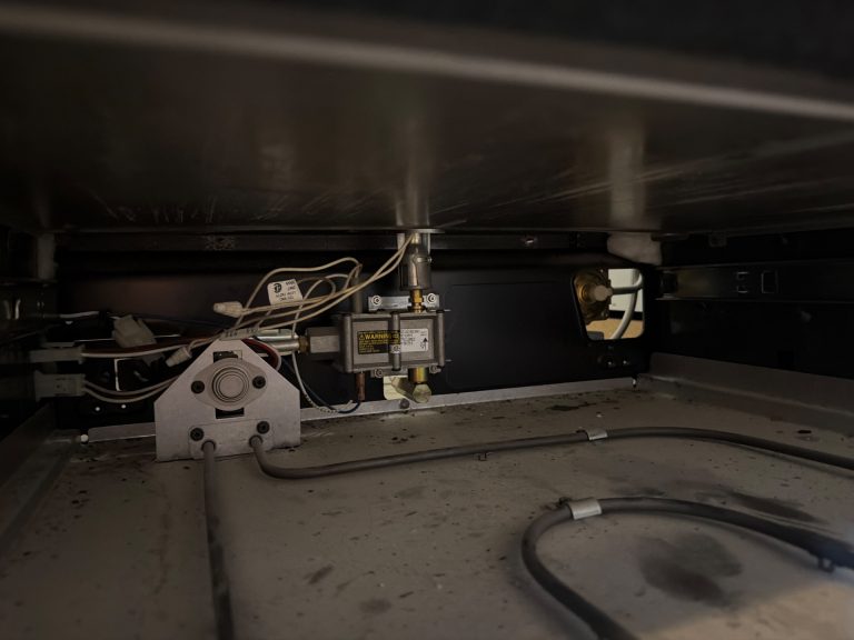 Inside a Frigidaire gas oven base showing the bake ignitor bracket, safety gas valve, and burner tube during TechVill diagnosis in Calgary