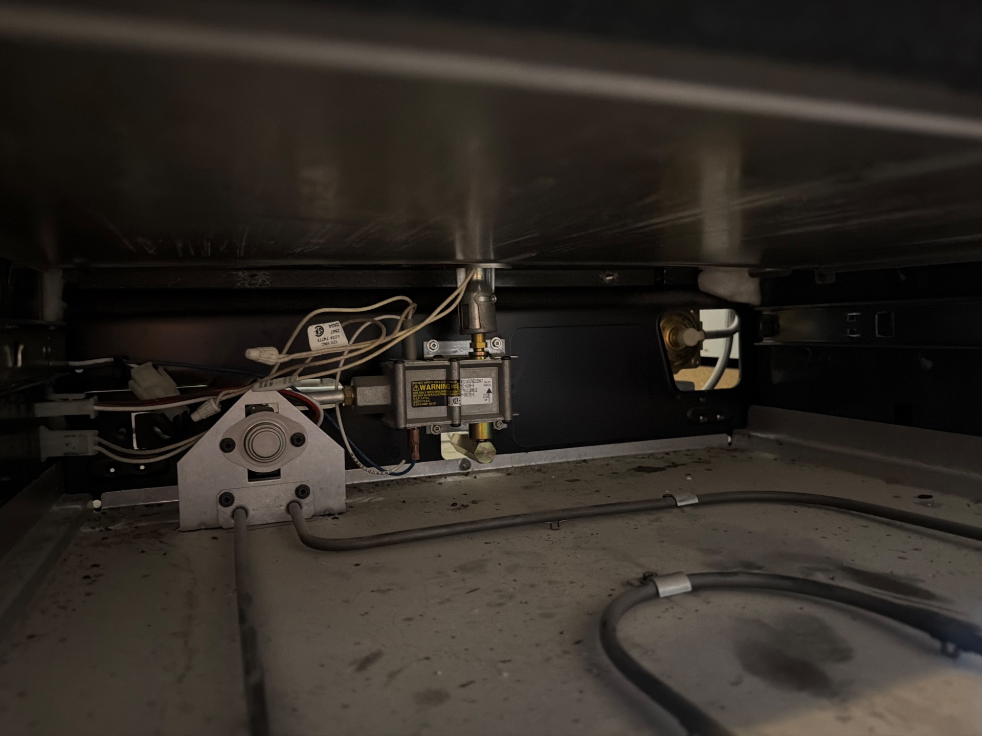 Inside a Frigidaire gas oven base showing the bake ignitor bracket, safety gas valve, and burner tube during TechVill diagnosis in Calgary