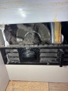Heavily dust-clogged condenser behind the kickplate grille of a Miele built-in refrigerator, cleaned on site by TechVill in Priddis, Alberta