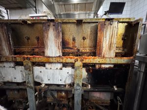 Exposed burner bank of a Frymaster gas fryer showing heavy grease accumulation and charred insulation areas