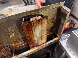 Panel from a commercial deep fryer coated in polymerized oil and grease buildup during deep cleaning in Vancouver
