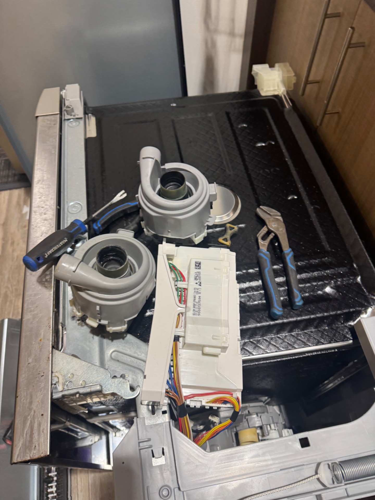 Removed Bosch dishwasher wash motor pump housings and control module laid out during a repair in Marlborough, NE Calgary