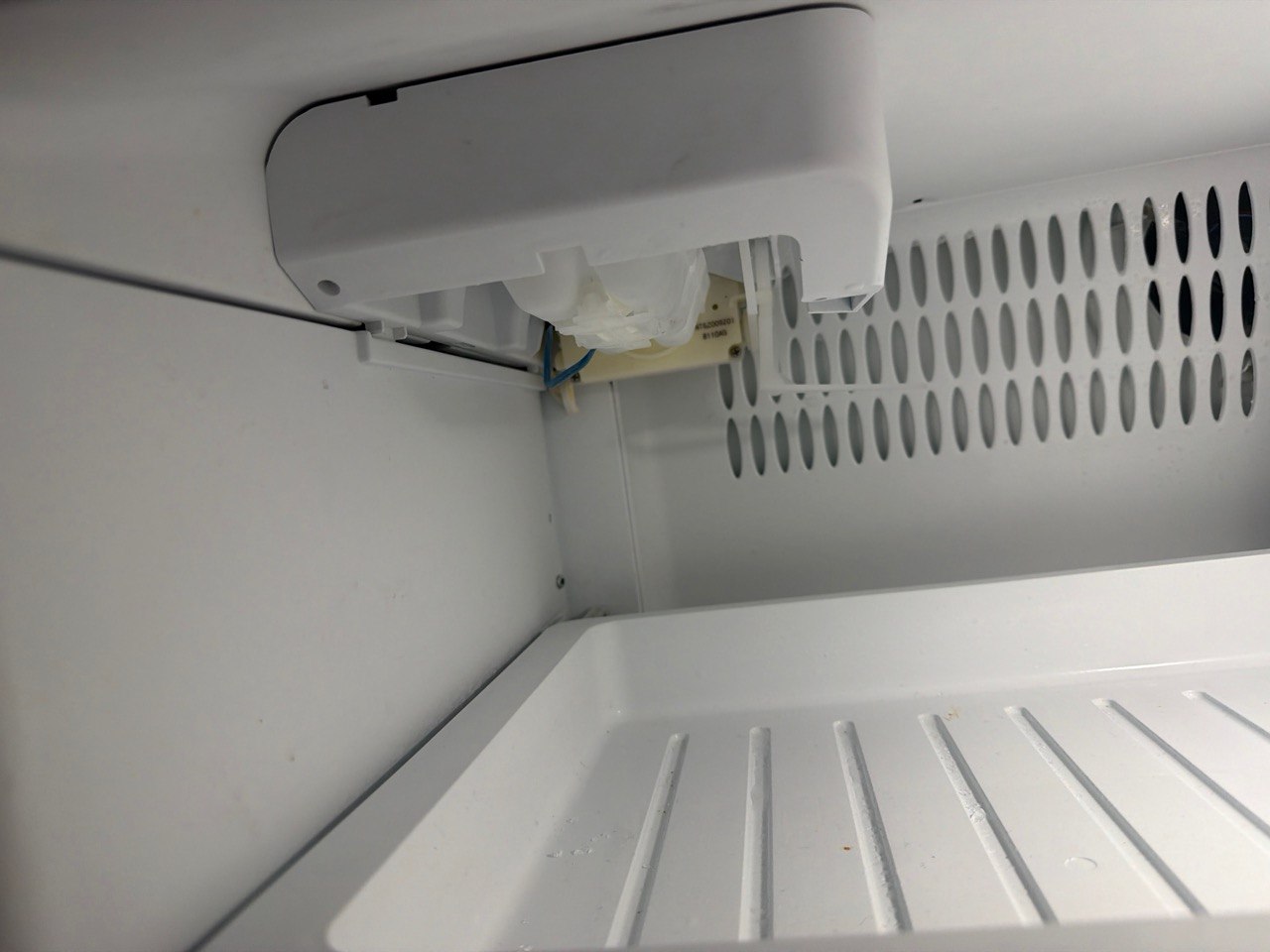 Close-up of the Fisher & Paykel ice maker assembly inside the freezer compartment with the cover removed, showing the frozen ice mould and ejector that failed to rotate during the harvest cycle