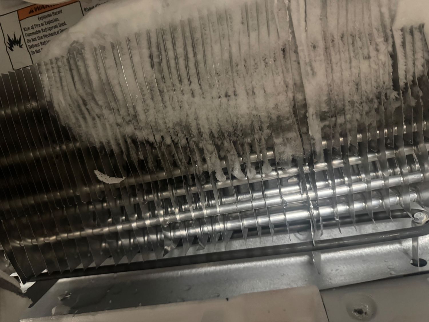 Whirlpool refrigerator evaporator coil with heavy frost concentrated on one side and bare tubing on the other, indicating a restricted sealed system