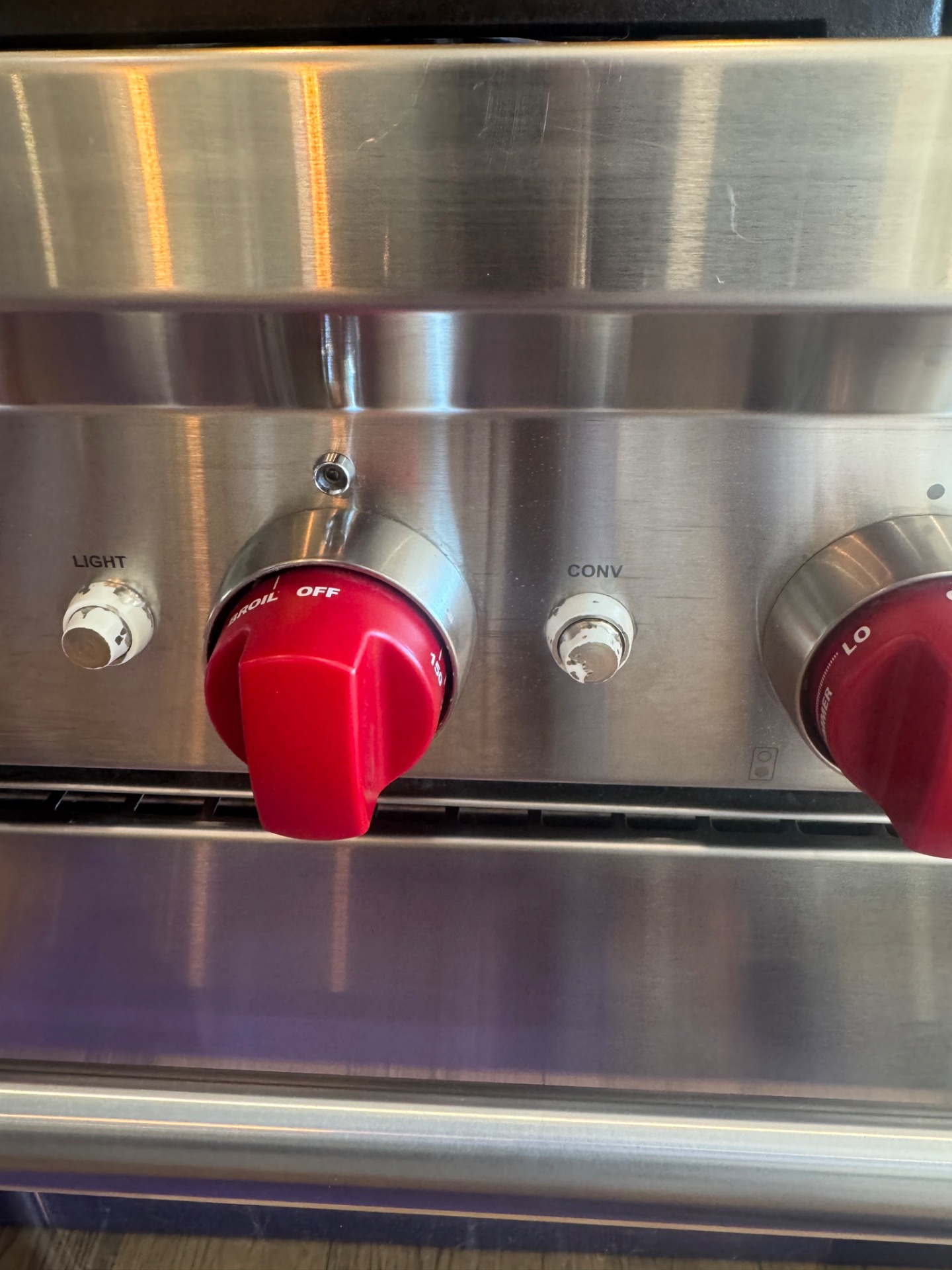 Close-up of a Wolf gas range control panel showing worn switch buttons with the coloured finish rubbed off, beside the BROIL/OFF dial