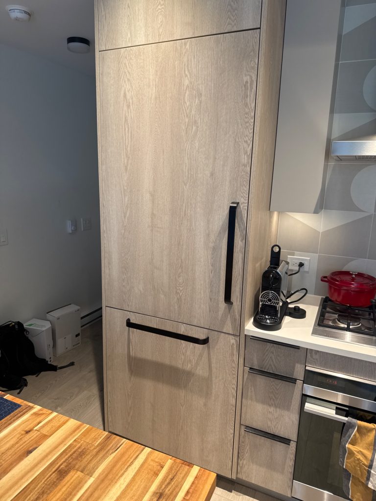 TechVill technician inspecting the freezer door sensor on a Fisher & Paykel integrated refrigerator in Vancouver
