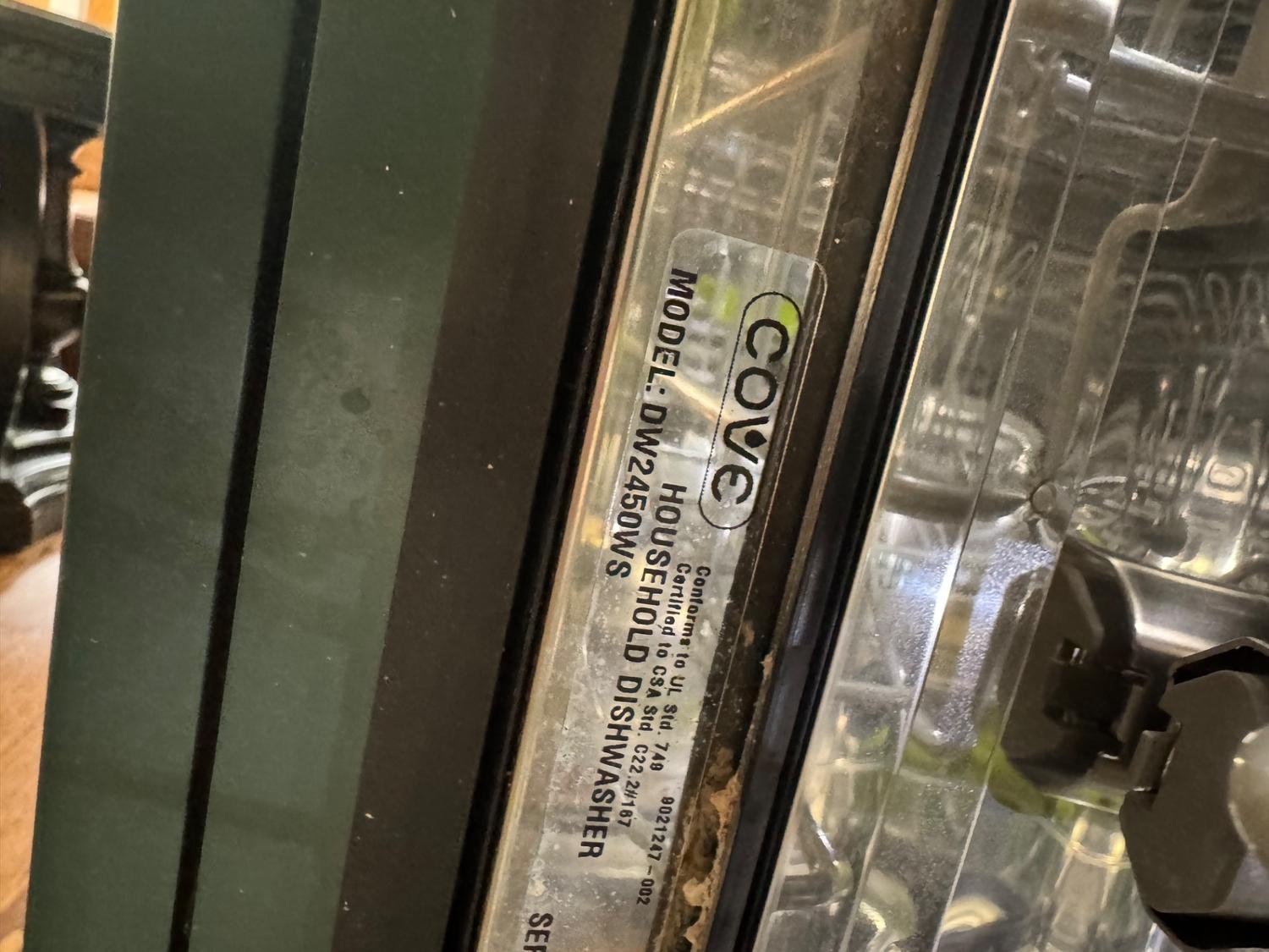 Cove DW2450WS model label inside the dishwasher door frame confirming the unit serviced in Canmore