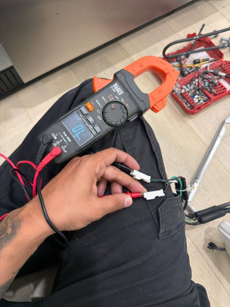 TechVill technician checking resistance across a refrigerator defrost heater with a clamp meter during a Calgary repair