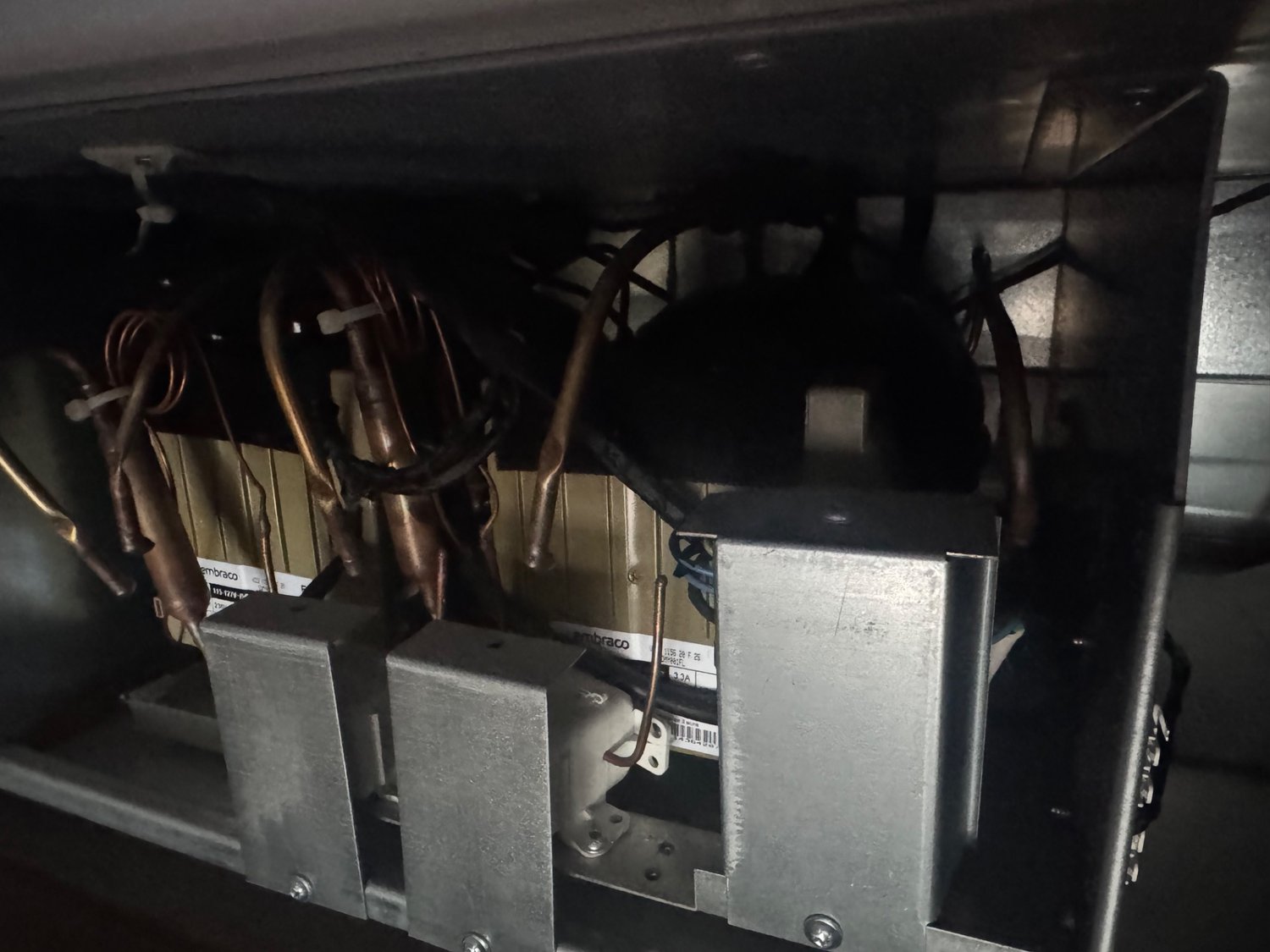 Machine compartment of a Thermador built-in refrigerator in Calgary showing dual compressors, inverter housings and refrigerant lines