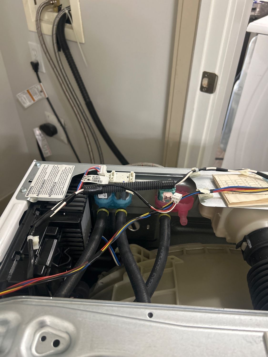 Top panel removed from a Whirlpool front-load washer in Calgary exposing the water inlet solenoid valves and wiring harness