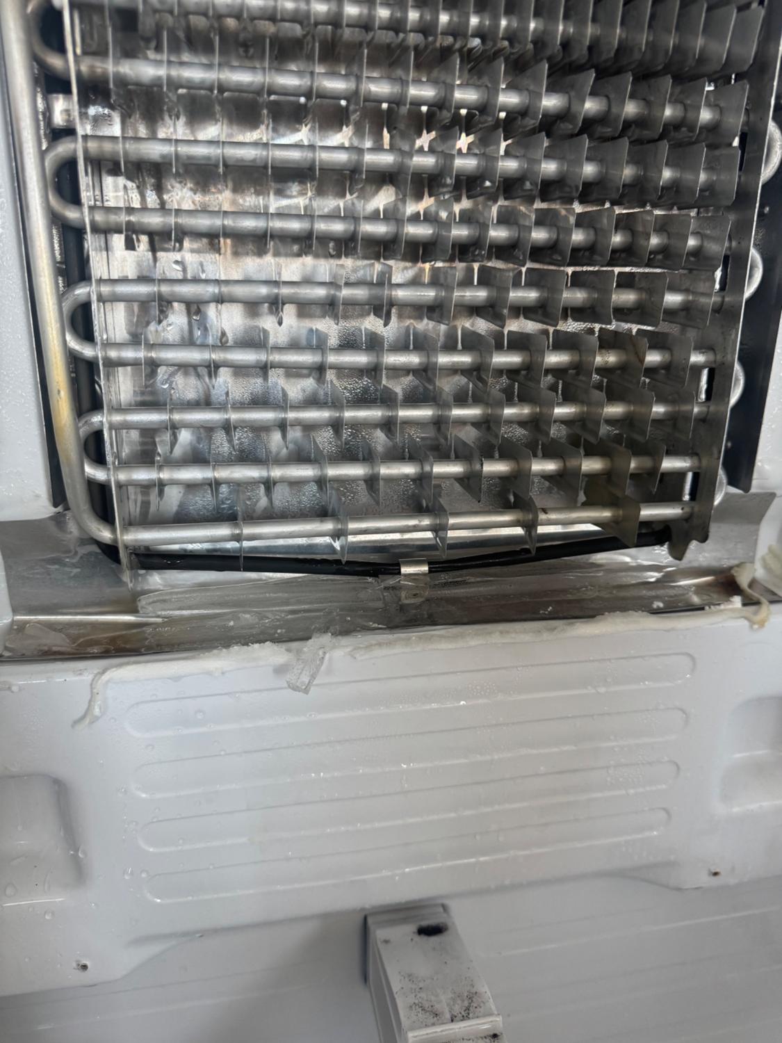 Exposed evaporator coil and drain trough inside a Samsung refrigerator with water pooling below the fins