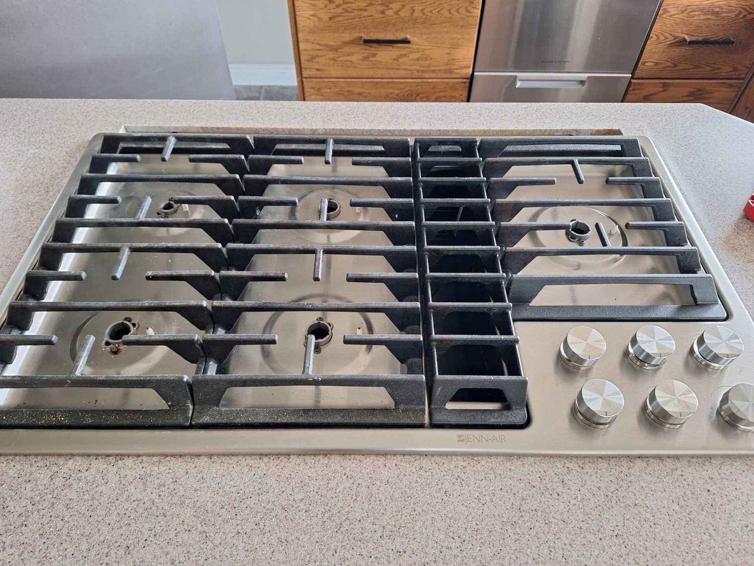 JennAir island downdraft cooktop in De Winton with all five cup burner assemblies missing from the burner wells