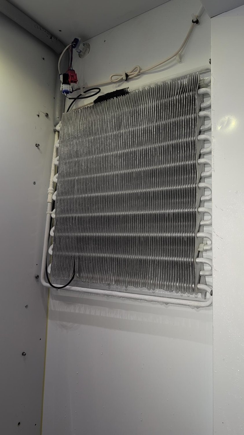 Exposed fresh food evaporator coil of a Bertazzoni refrigerator after the ice was cleared, with defrost wiring and sensor visible