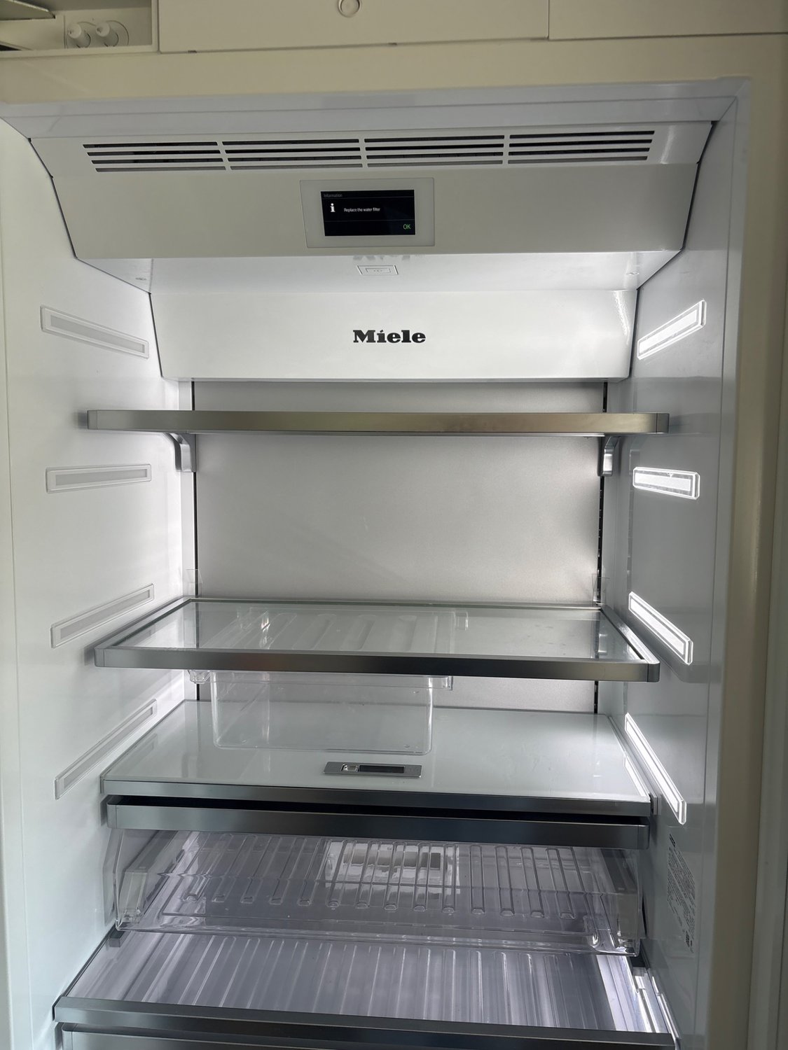 Interior of a Miele built-in refrigerator in rural Alberta with the control display showing a water filter reminder